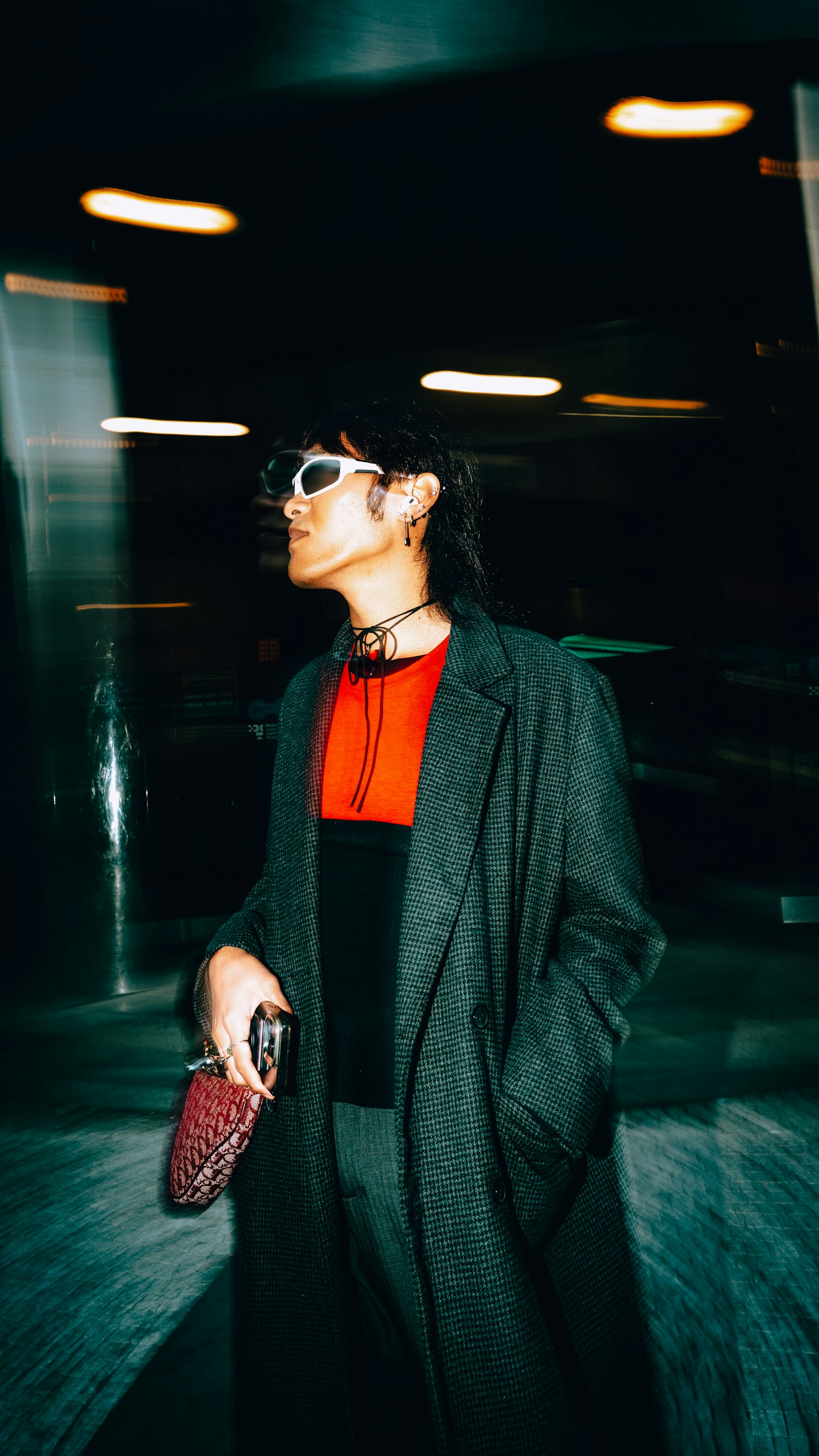 Editorial fashion model in a tailored black coat and bright scarf, lit in deep teal