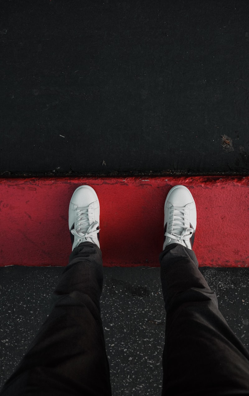 Feet in white VOLTA sneakers on red pavement